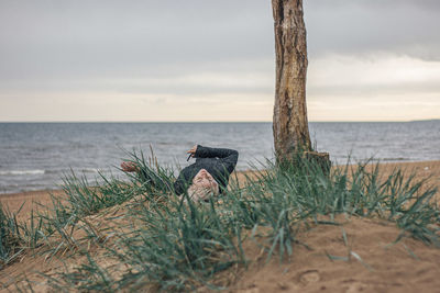 Man sitting on shore at beach against sky