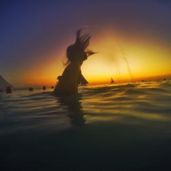Silhouette of woman in sea at sunset