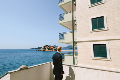 Rear view of man standing by building against sky