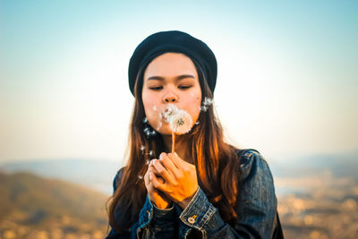 Portrait of young woman holding camera against sky during sunset