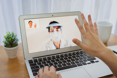 Friend video conferencing doctor on laptop at table