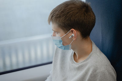 A young man eats in a public place looks out the window, in a medical mask