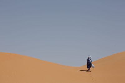 Man on sand dune in desert against clear sky