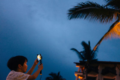 Side view of boy photographing from mobile phone on monopod against sky