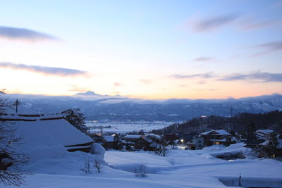 Snow covered houses by mountain against sky during sunset