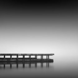 Reflection of pier in sea against sky during foggy weather