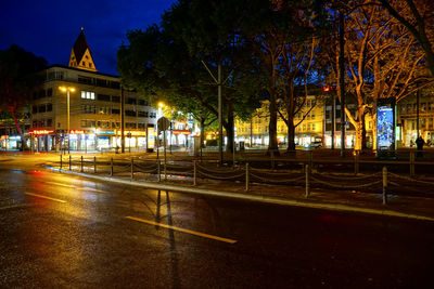Illuminated street by buildings at night