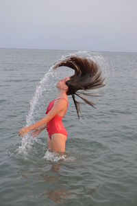 Side view of girl tossing hair while standing in sea against clear sky