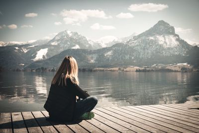 Woman sitting on lake by mountains against sky