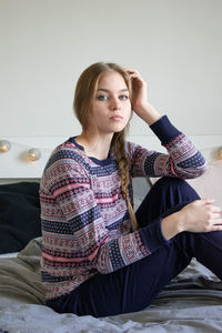 Young woman looking away while sitting on bed at home