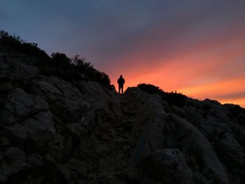 Silhouette person on rock against sky during sunset