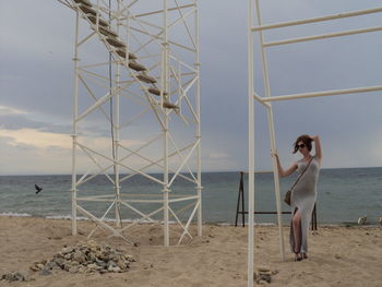 Young woman with hand in hair standing by lookout tower at sandy beach