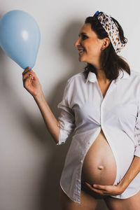 Midsection of a young woman holding balloons against wall