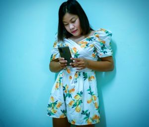 Young woman holding smart phone while standing against blue sky