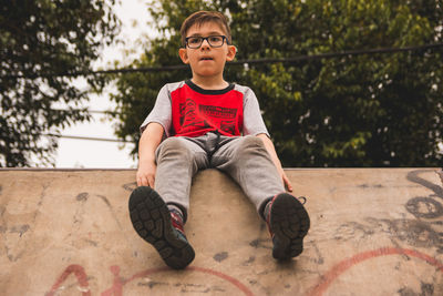 Low angle view of boy sitting on concrete wall