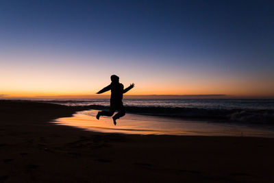 Silhouette boy jumping at beach against sky during sunset