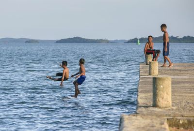 Boys diving into sea with friends against sky