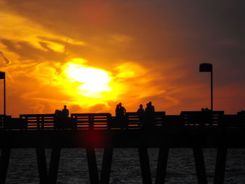 Silhouette people on pier by sea against orange sky