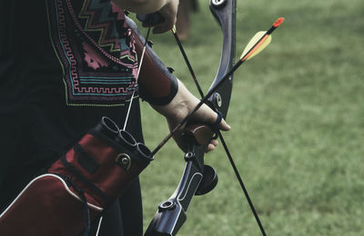 Midsection of woman holding bow and arrow on field