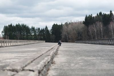 Man walking on road amidst trees against sky