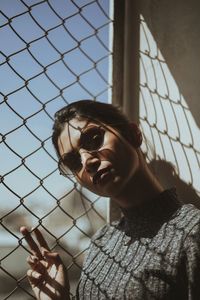 Portrait of woman standing against chainlink fence