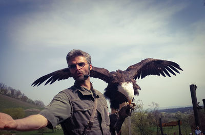Mature man feeding bald eagle against sky