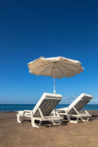 Deck chairs on beach against clear blue sky