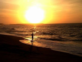 Full length of silhouette woman standing on shore at beach against sky during sunset