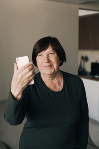 Senior woman using smart phone standing at home