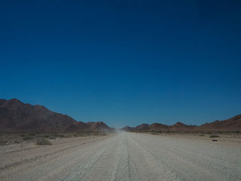 Scenic view of desert road against clear blue sky