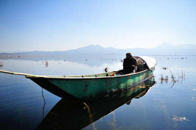 Man sitting in moored boat at lake against clear sky