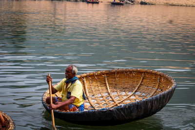 Man sitting in basket by boat in lake