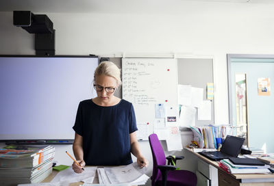 Teacher examining papers against blank whiteboard in classroom