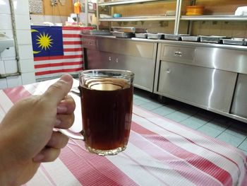 Close-up of hand holding coffee in glass on table