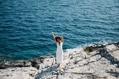 Full length of woman standing by sea on rock