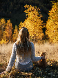 Rear view of woman sitting on tree during autumn