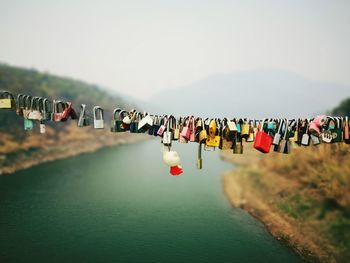 Padlocks hanging on bridge over river against sky