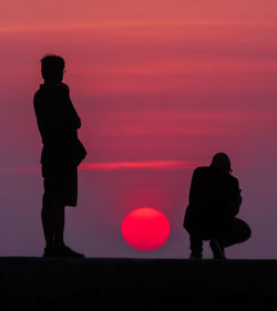 Silhouette couple standing against orange sky during sunset