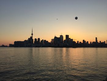 Lake ontario against cn tower amidst buildings during sunset