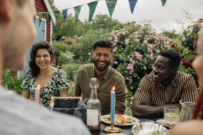 Man laughing while sitting at table with male and female friends during party