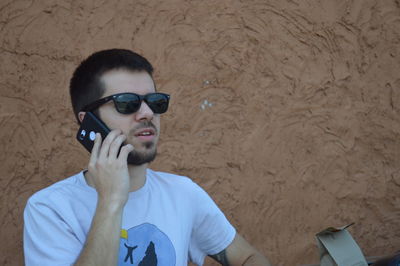 Young man wearing sunglasses while standing against wall