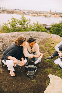 High angle view of female friends reading paper while preparing barbecue on field