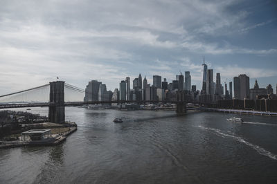 Bridge over river by buildings in city against sky