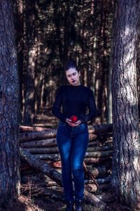 Portrait of spooky woman holding apple while standing by tree trunk in forest