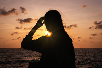 Silhouette woman by sea against sky during sunset