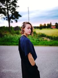 Young woman looking away while standing on road against sky