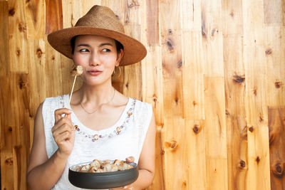 Portrait of young woman holding ice cream against wall