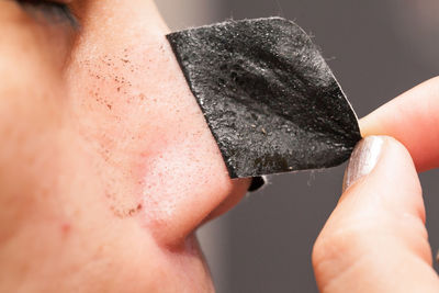 Close-up midsection of woman removing black facial mask from nose