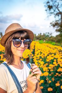 Portrait of smiling young woman holding flower on field