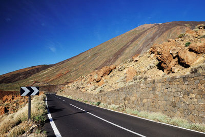 Empty road along rocky landscape against blue sky